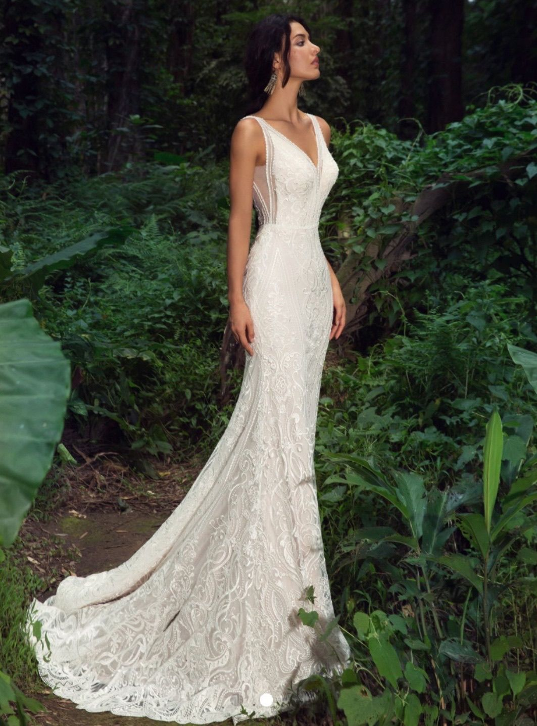 Woman in a white lace wedding dress poses in a forest setting.