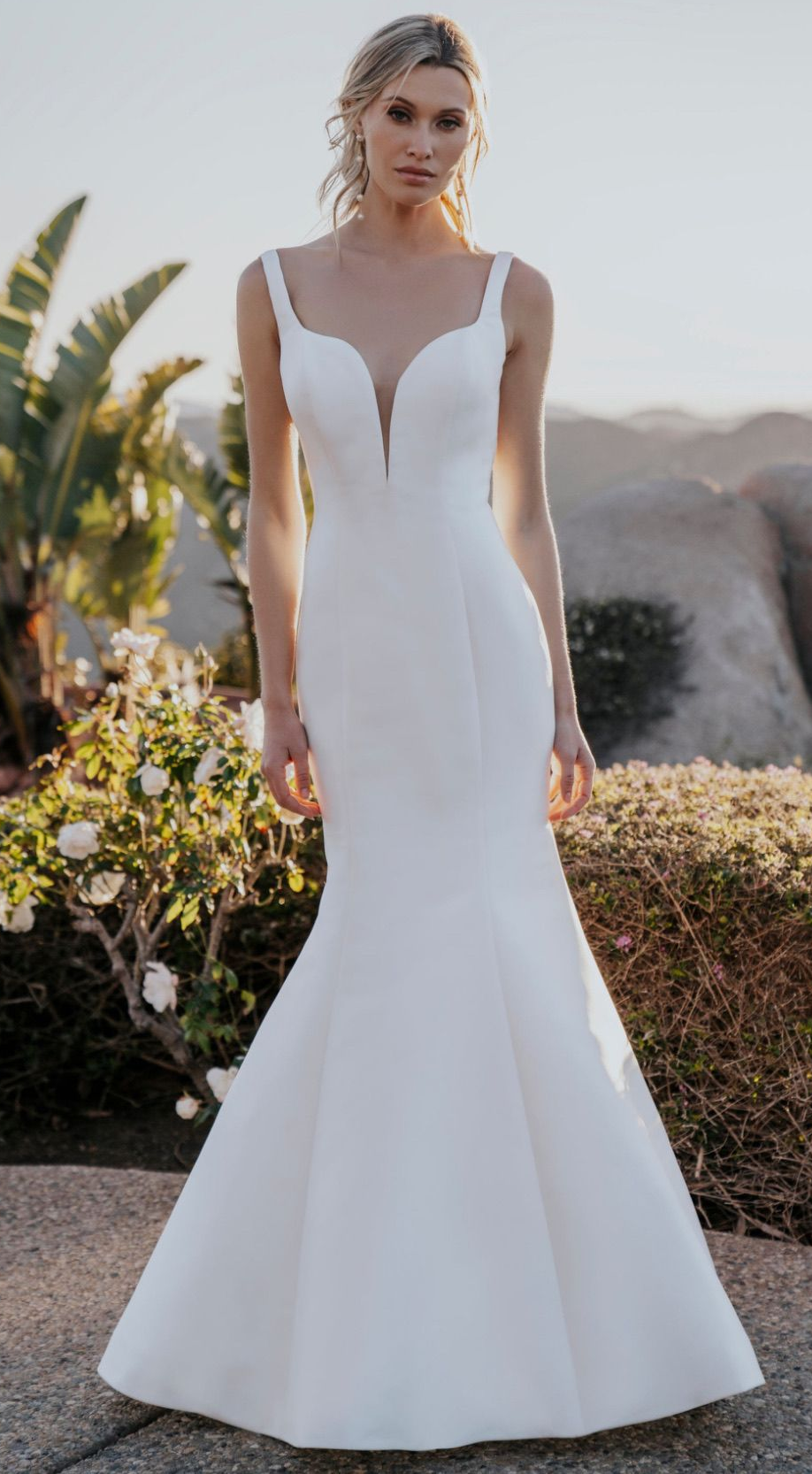 Woman in a white mermaid-style wedding dress, posing outdoors.