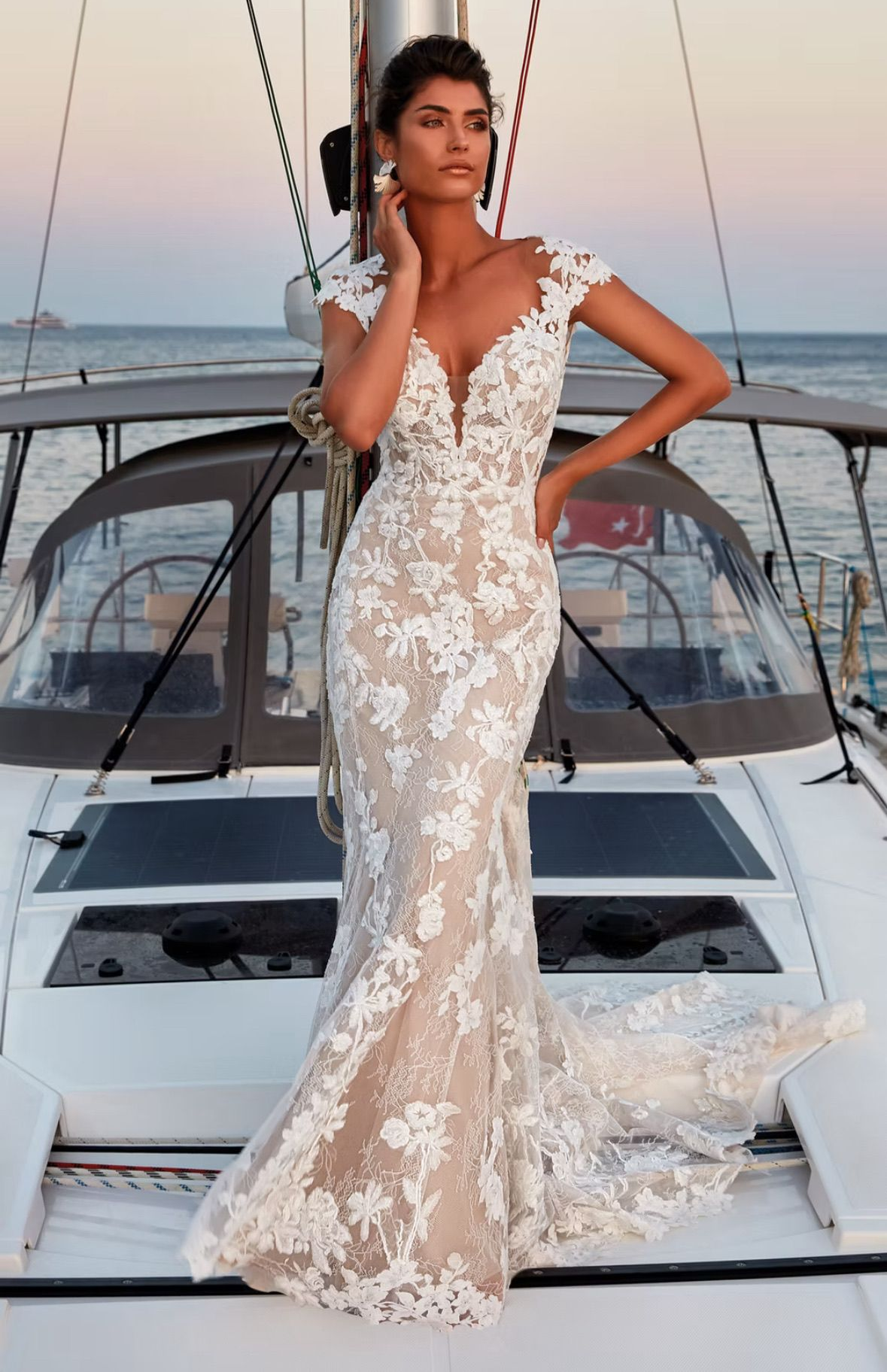 Woman in a white lace wedding dress poses on a yacht, smiling at sunset.