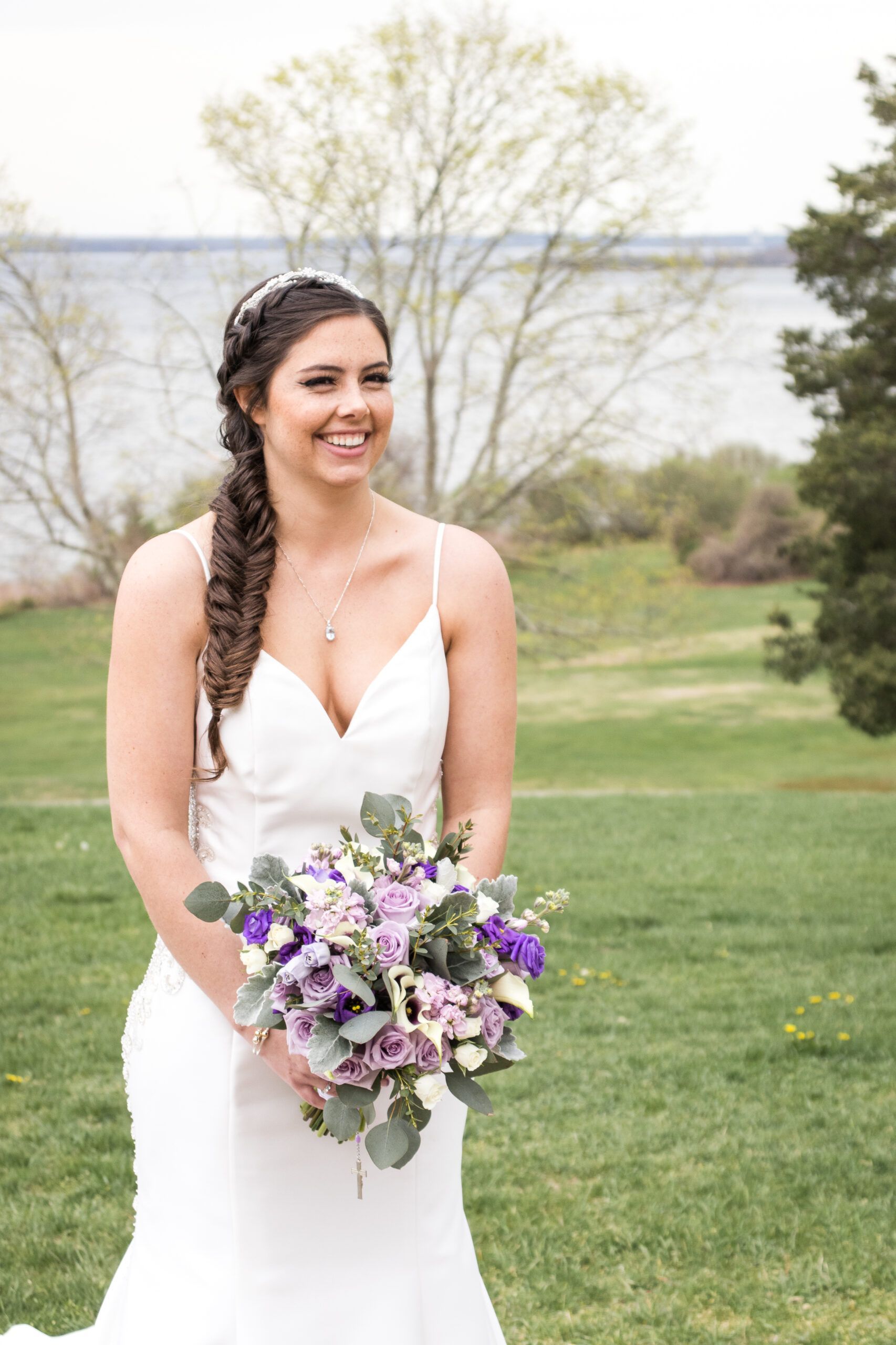 A bride in a white dress is holding a bouquet of purple flowers.