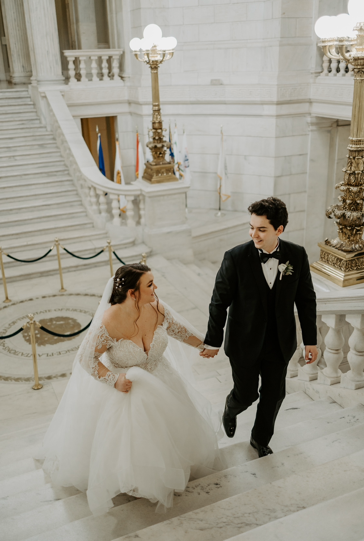 A bride and groom are walking down a set of stairs holding hands.