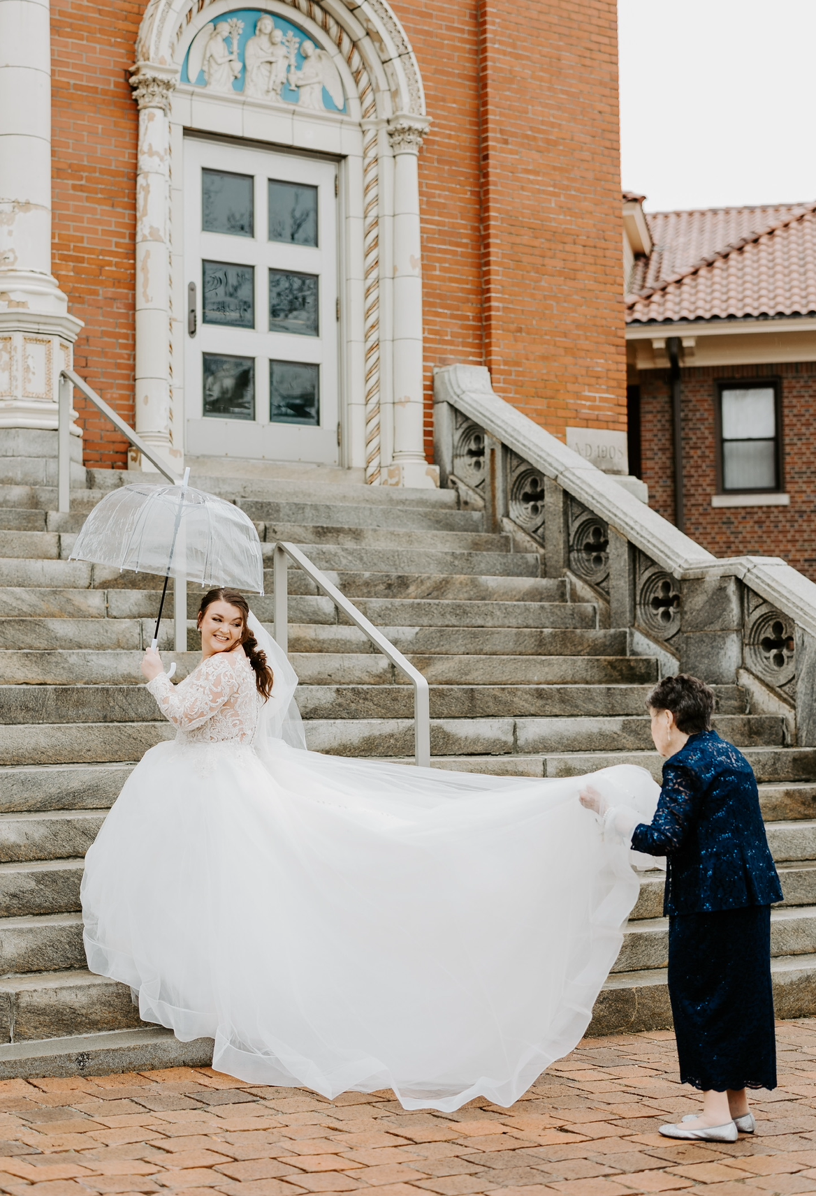 A bride in a wedding dress is standing on a set of stairs holding an umbrella.