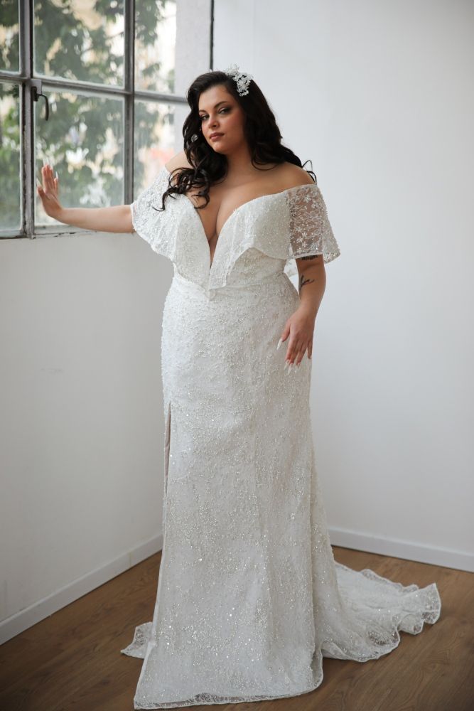 A woman in a white wedding dress is standing in front of a window.
