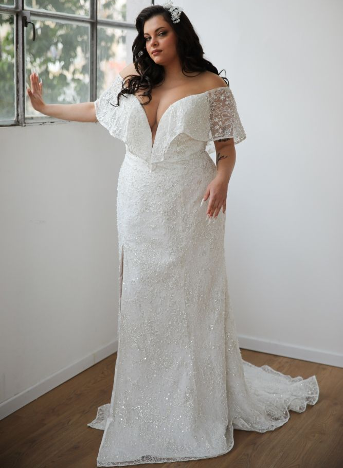A woman in a white wedding dress is standing in front of a window.