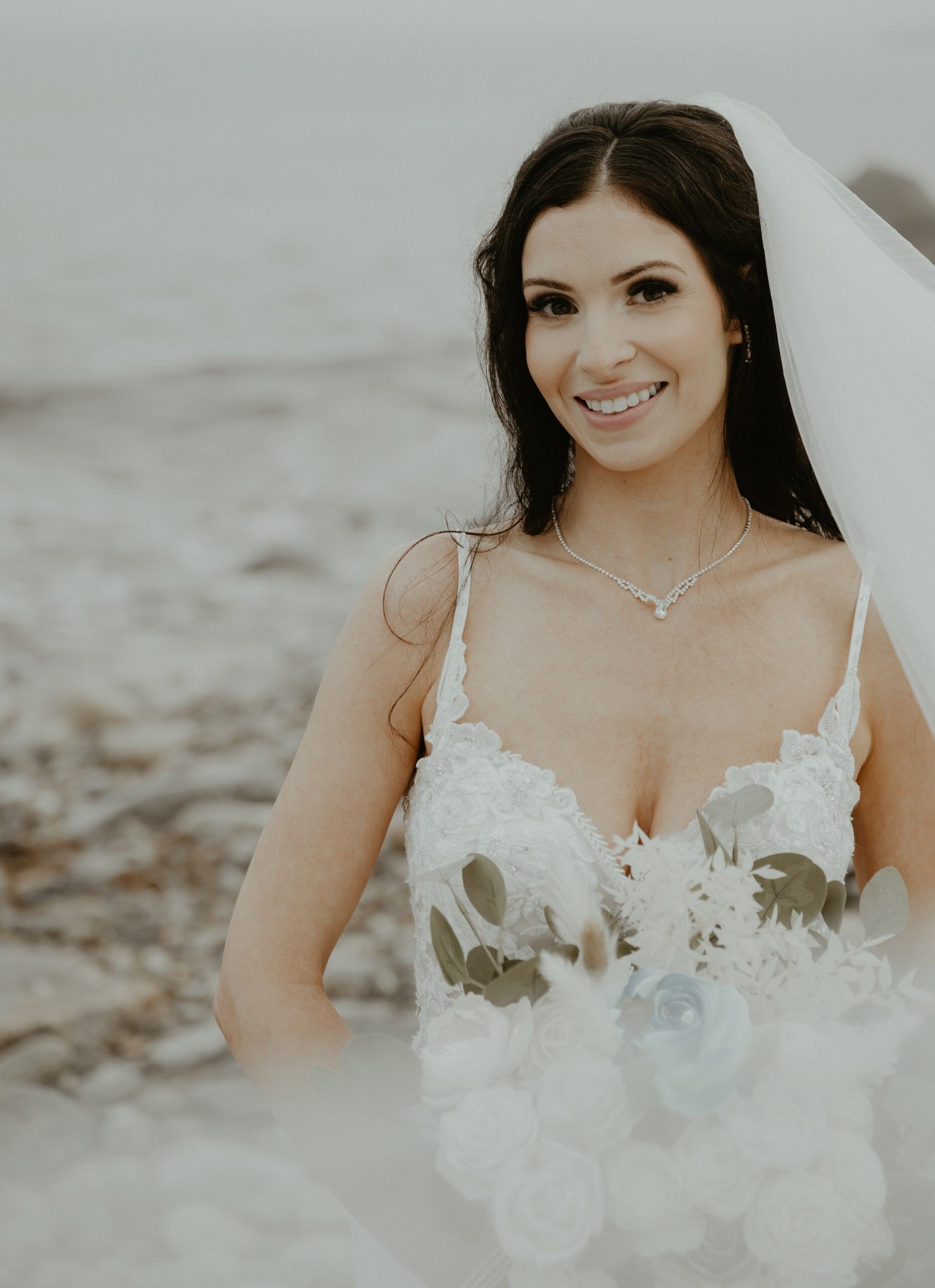 A woman in a wedding dress and veil is standing on the beach.