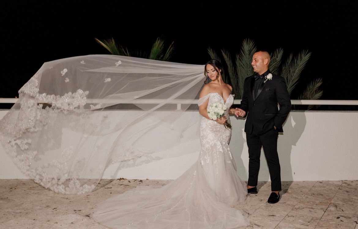 A bride and groom are standing next to each other on a balcony at night.