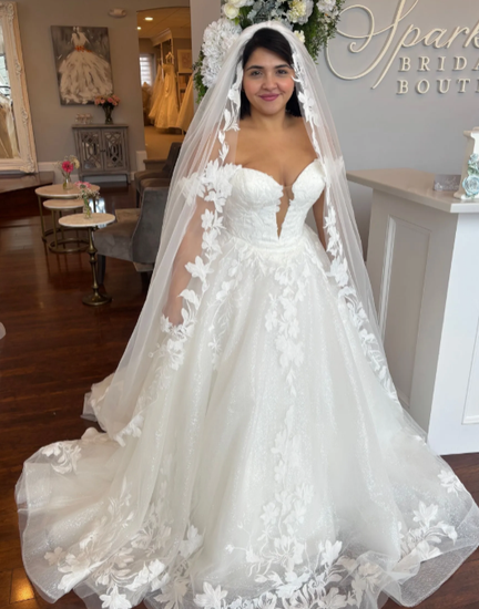 A woman is wearing a white strapless wedding dress in a bridal shop with veil.
