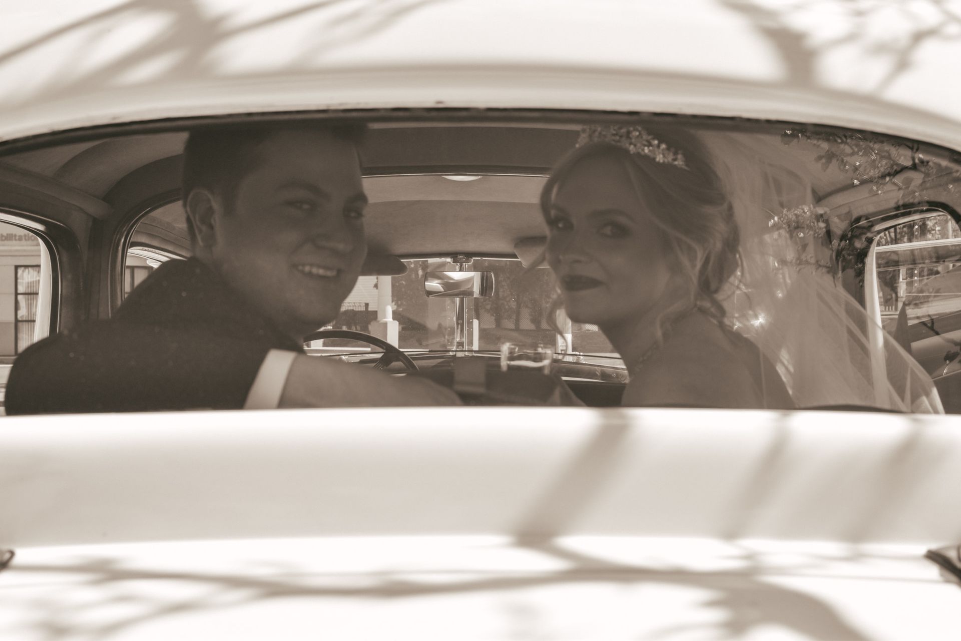 A bride and groom are sitting in a car looking out the window.