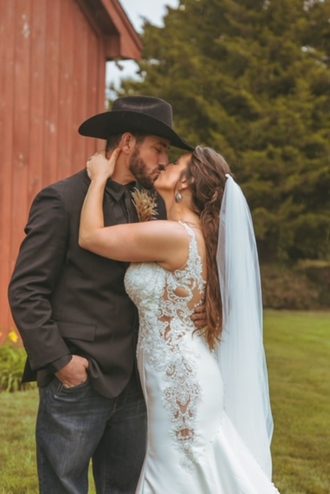 A bride and groom are kissing in front of a red barn.