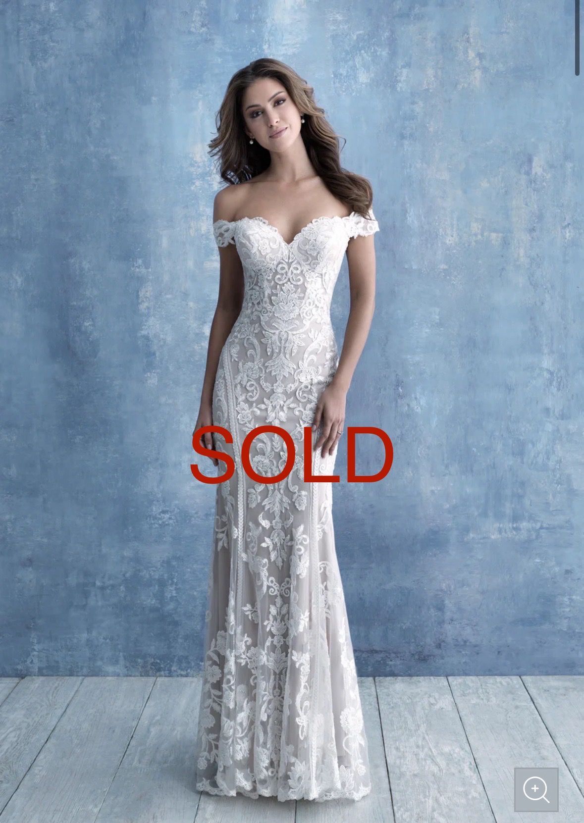 Woman in an off-shoulder white lace wedding dress, posing in front of a blue textured wall.