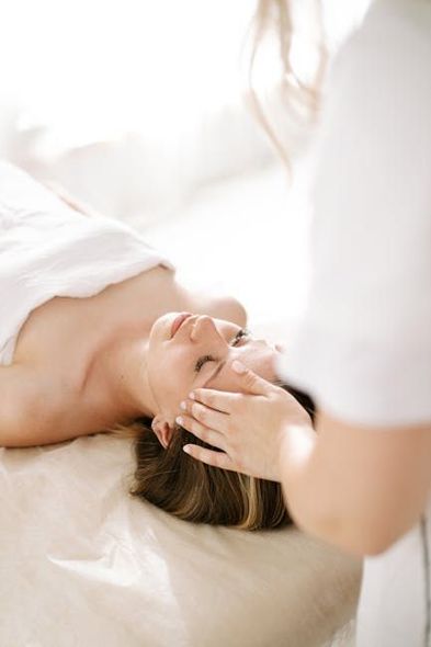 Woman receiving a facial massage, laying on a table, by a person in white.