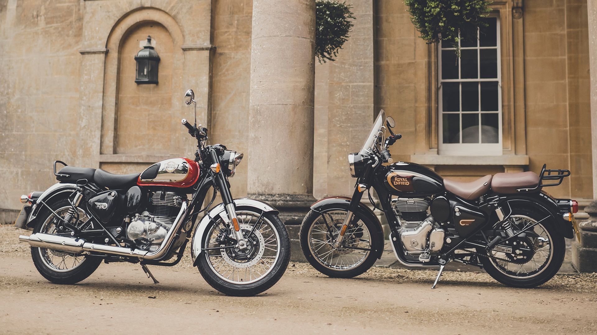Two Royal Enfield motorcycles parked in front of a building with columns and a window.