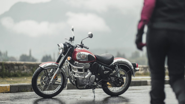 Red-and-black motorcycle parked on a wet road beside a blurred person in a misty outdoor setting