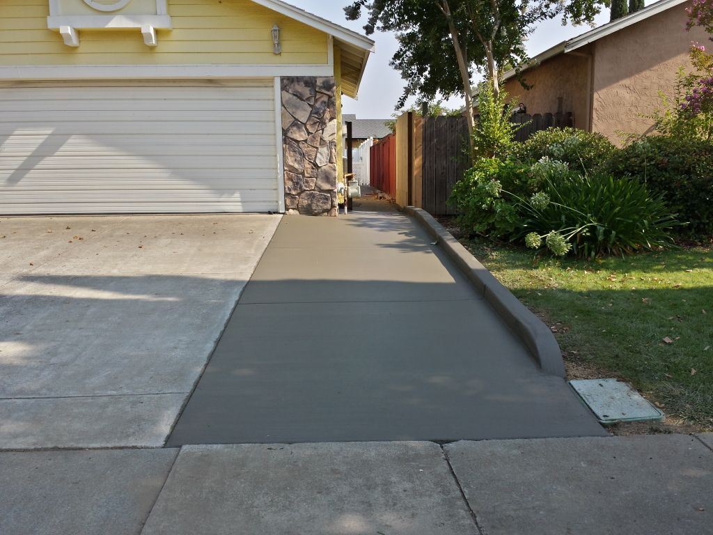 A concrete driveway leading to a yellow house