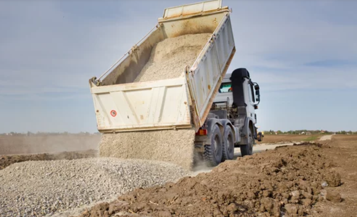 A dump truck is dumping dirt on a dirt road.