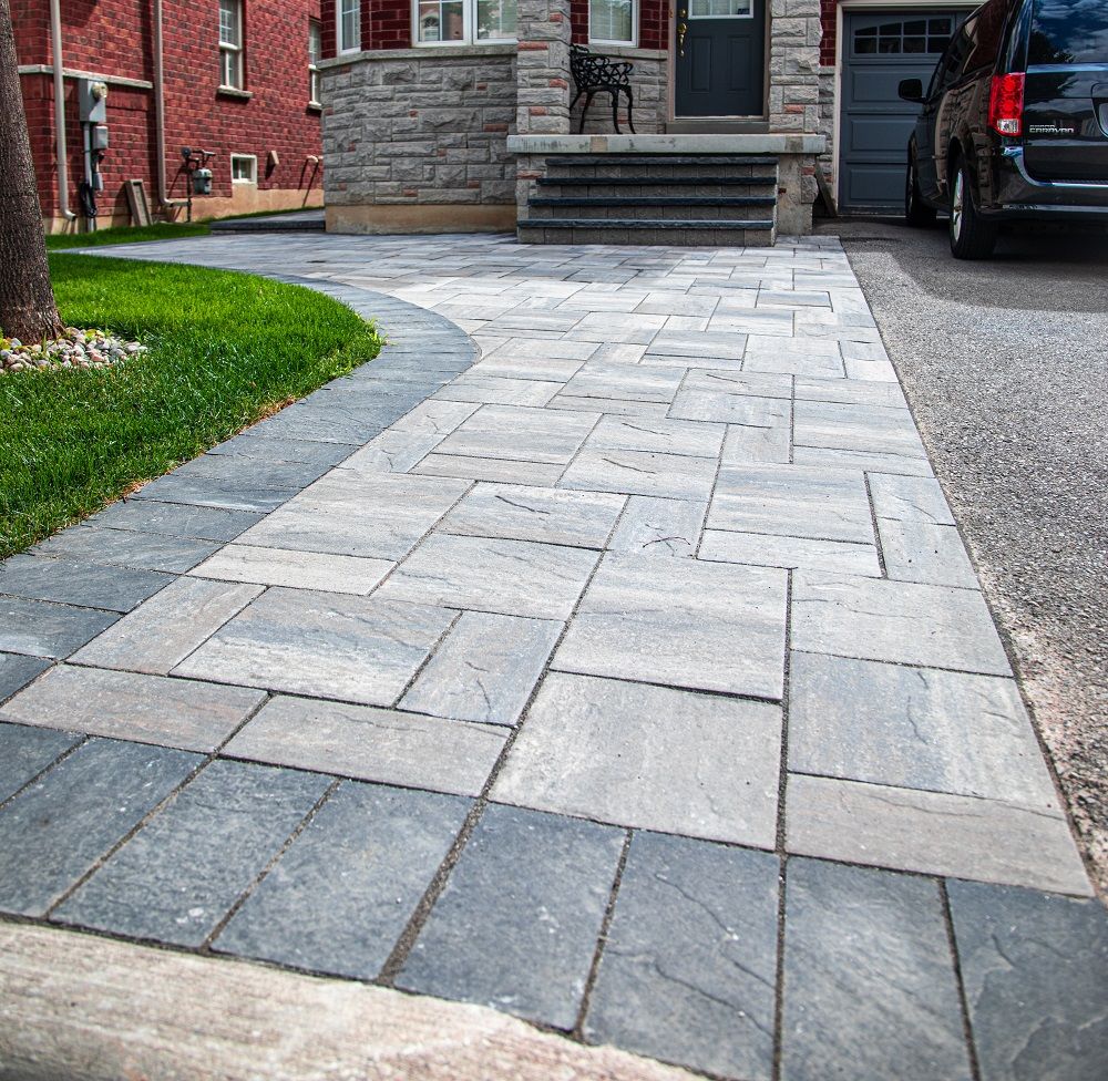 A brick walkway leading to a house with a car parked in front of it