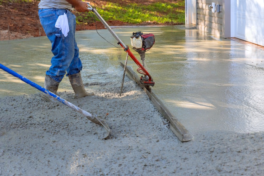 A man is spreading concrete on a driveway with a machine.