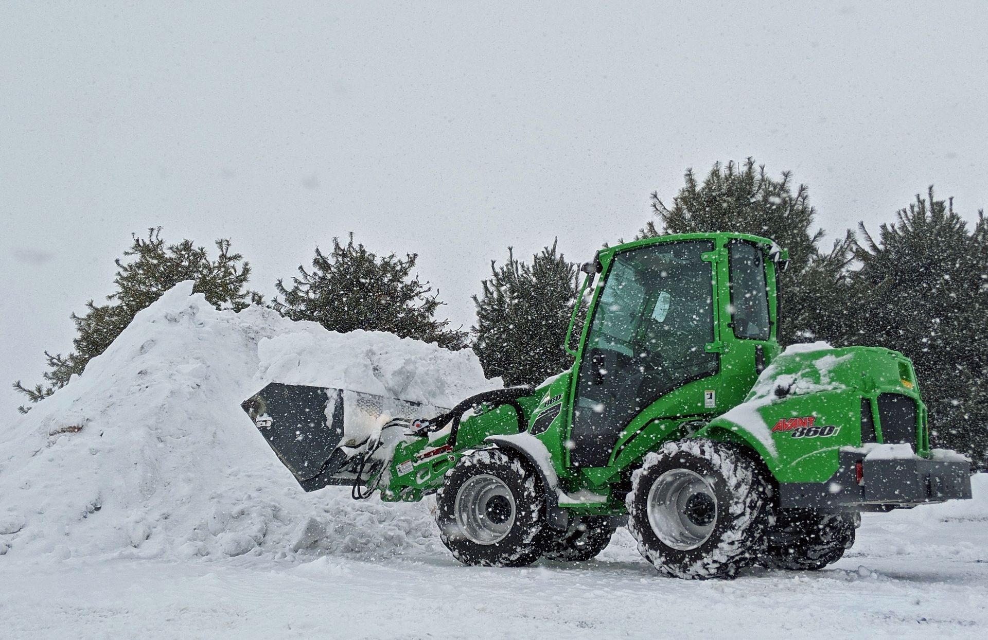 A green tractor is clearing snow from a pile of snow.