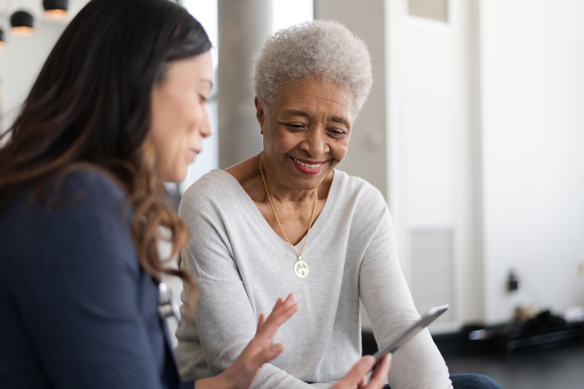 Two women are sitting next to each other looking at a tablet.