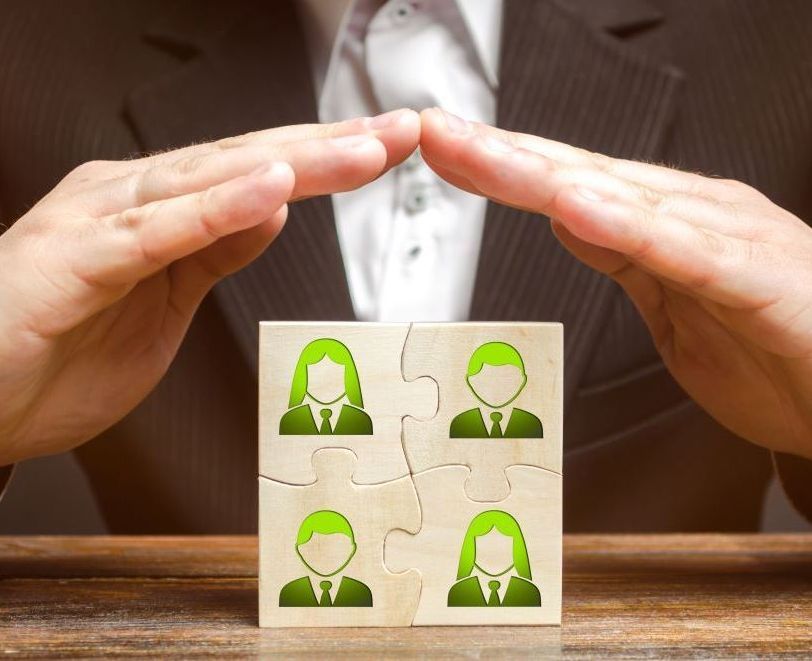 A man in a suit is covering a wooden puzzle with green people on it.