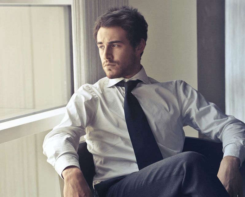 A man in a white shirt and tie is sitting in a chair in front of a window.