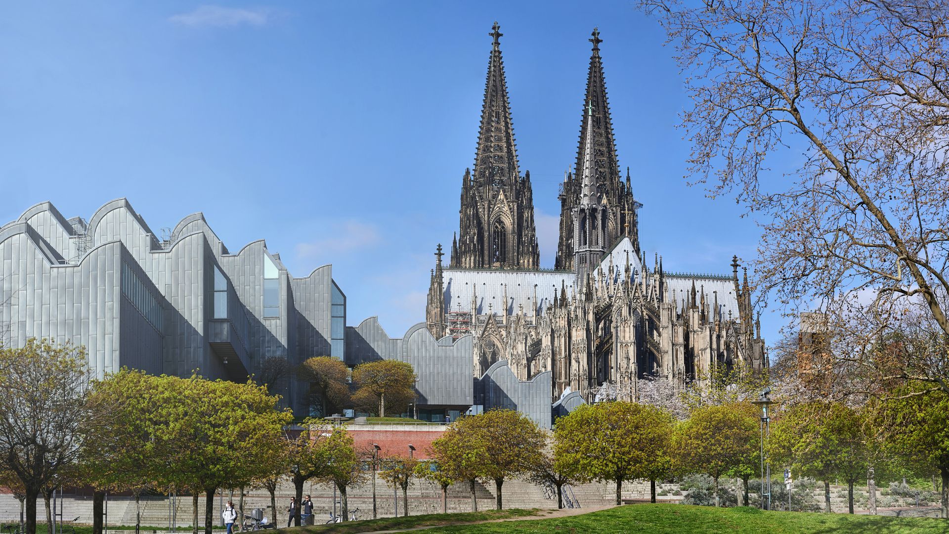 A large building with two towers is surrounded by trees and a park.