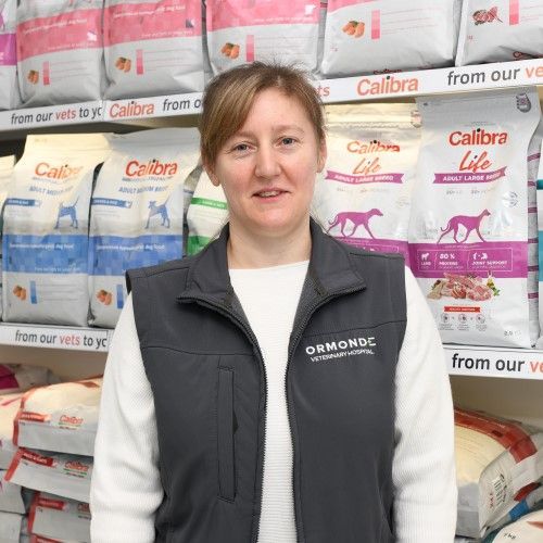 Woman in a vet clinic, standing in front of dog food, wearing a vest that says 