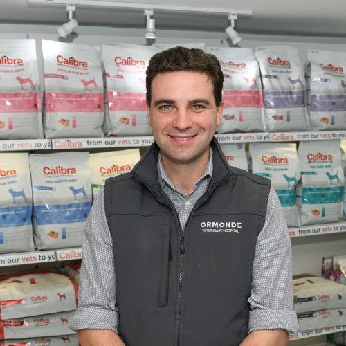 Man in gray vest smiles in front of Calibra pet food. 