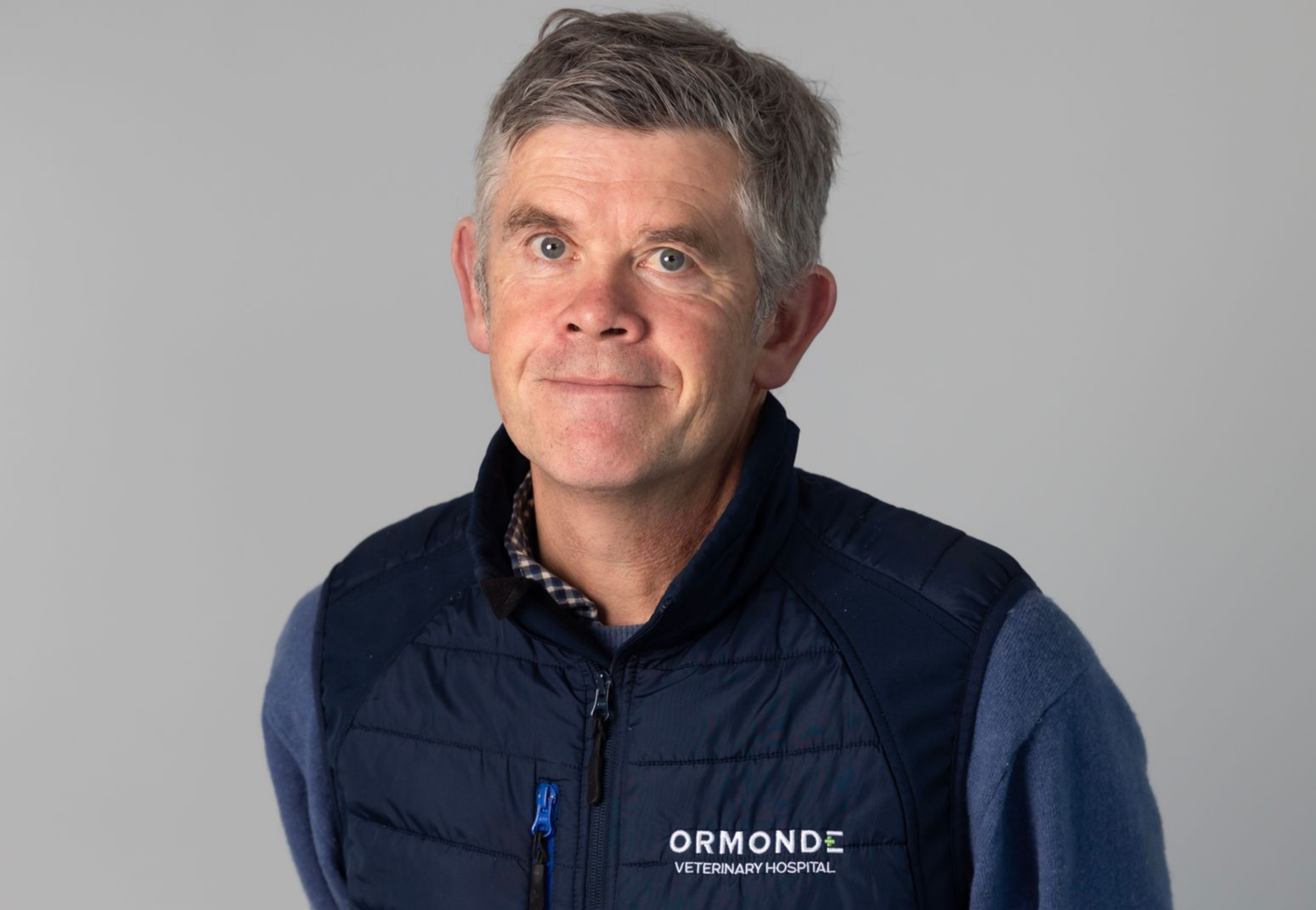 Man in gray vest, light blue shirt, outside, looking at camera.