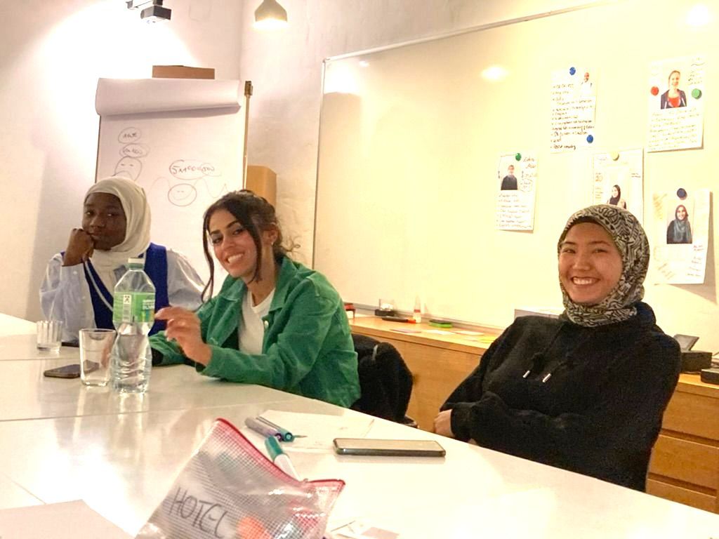 3 junge lächelnde Frauen am Tisch mit Arbeitsmaterial