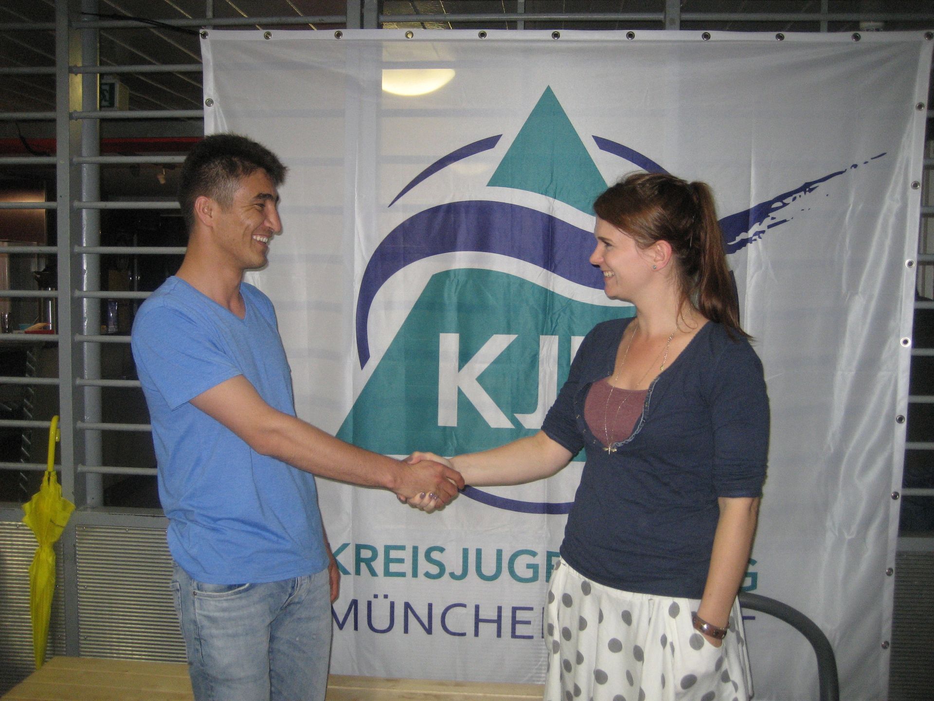 Junger Mann und junge Frau Handshake vor dem Poster des KJR