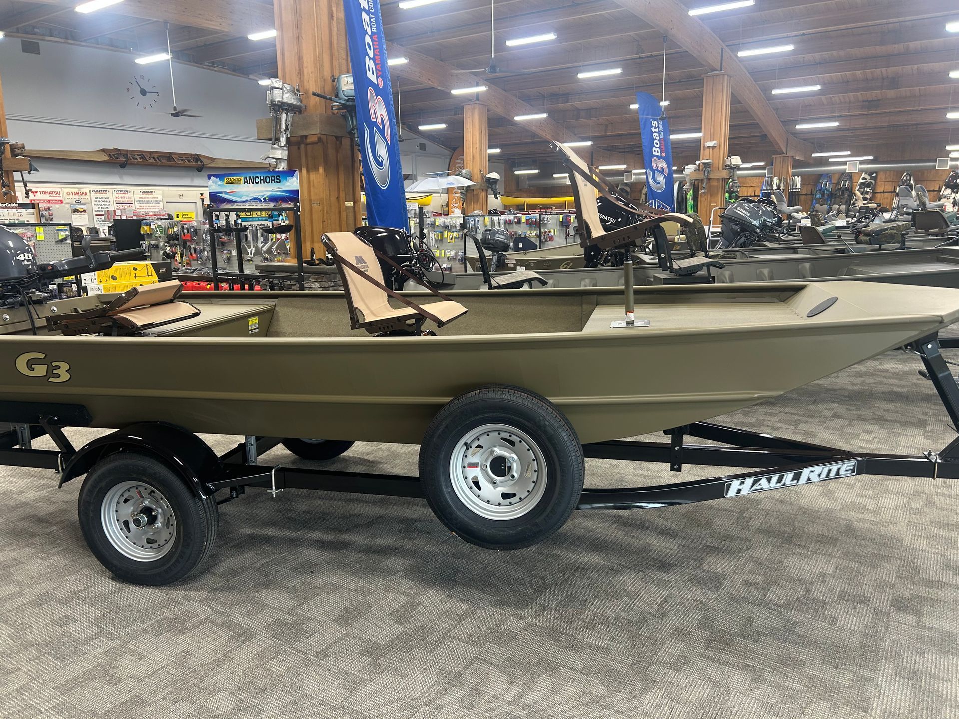 A tan G3 flat-bottom fishing boat on a trailer inside a retail showroom.