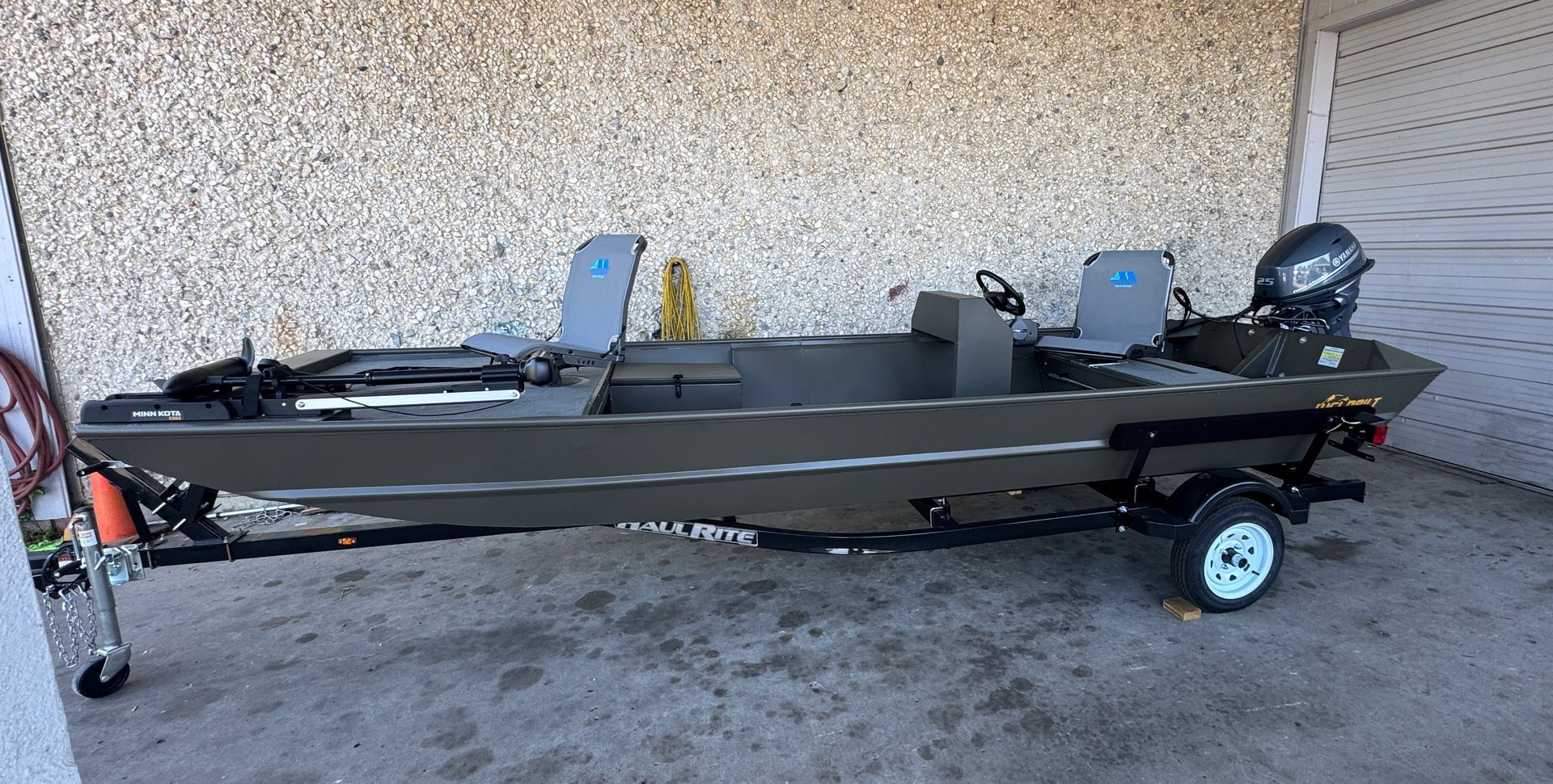 A boat is parked on a trailer in front of a stone wall.