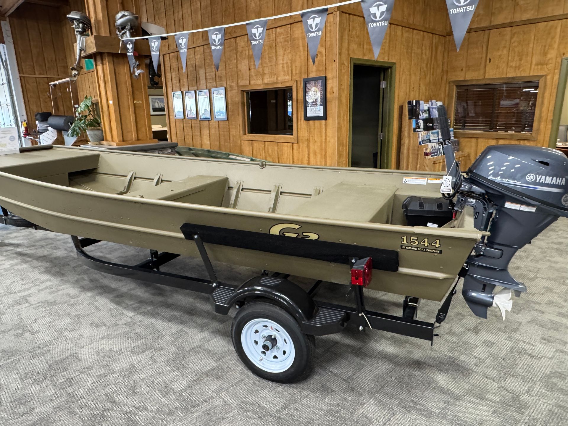 A tan-colored aluminum jon boat with a black motor on a trailer, inside a store.