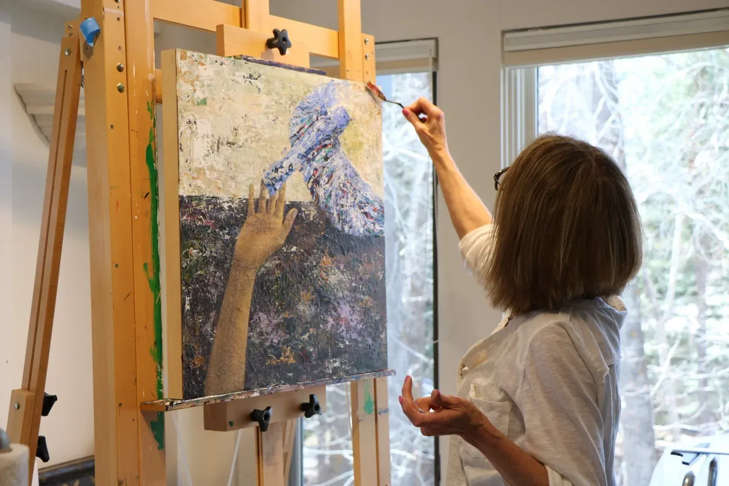 Artist applying paint to canvas on an easel, using a palette knife. Interior studio, natural light.