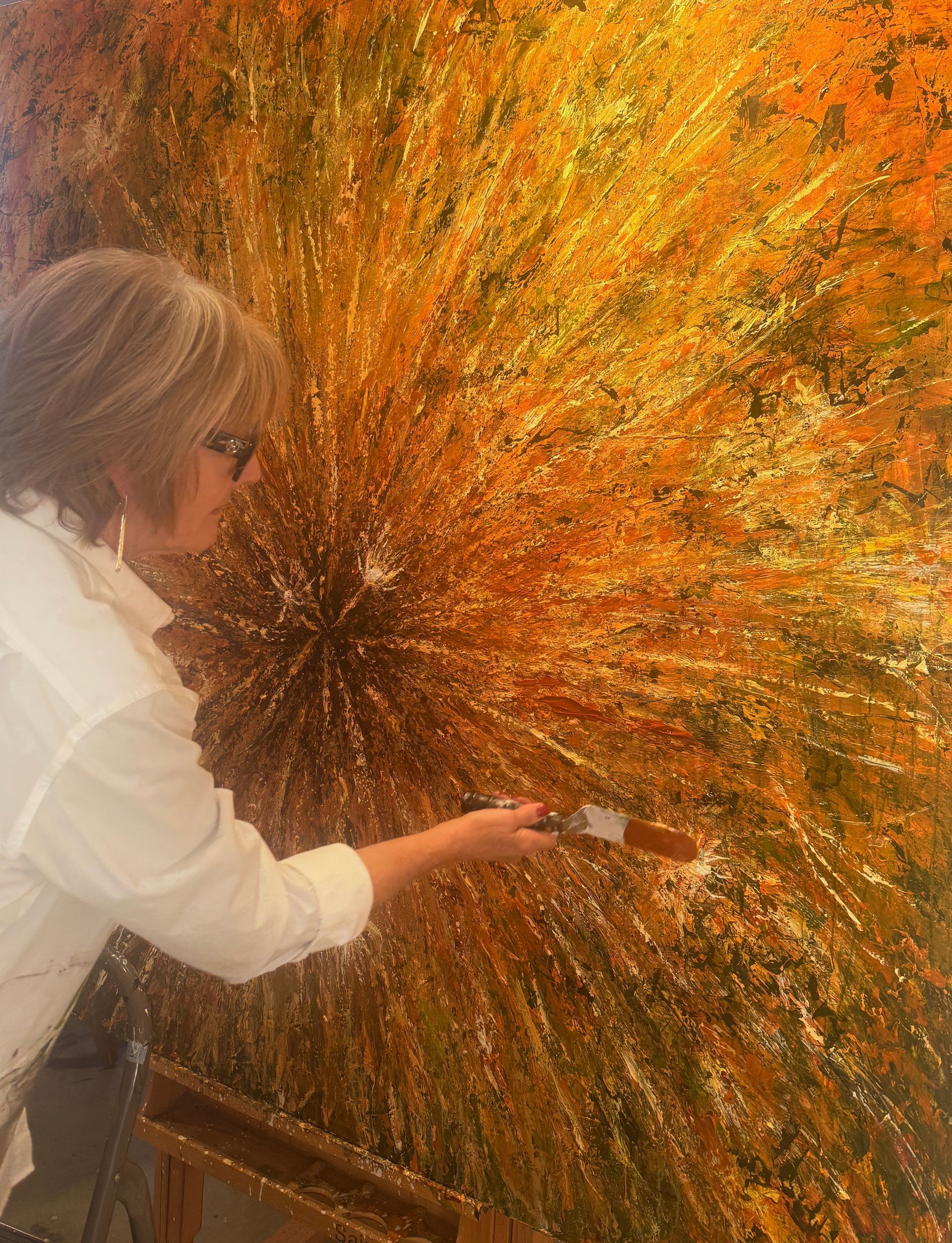Woman painting a large, abstract canvas with a burst of orange and gold.