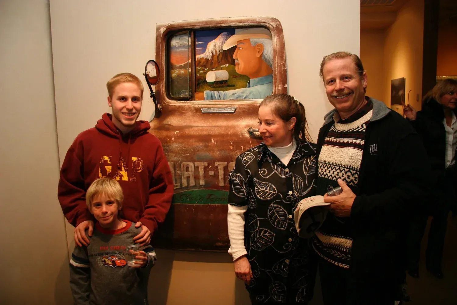 Family poses with a rusty-toned art piece of a gas pump, in a gallery setting.