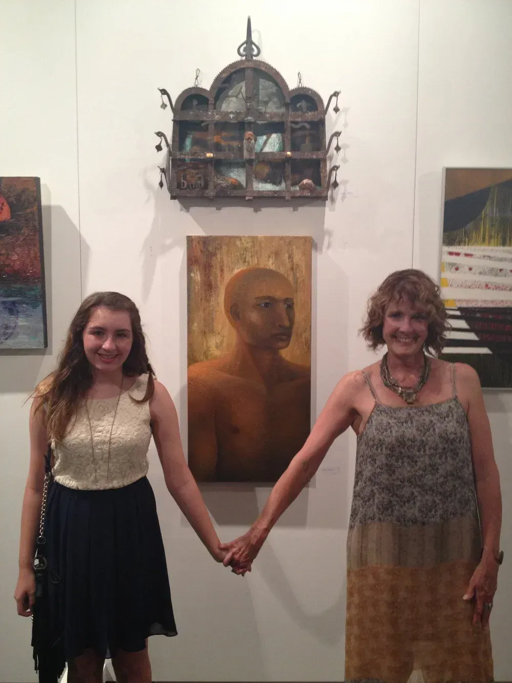 Two women holding hands in front of a painting. They are at an art gallery.