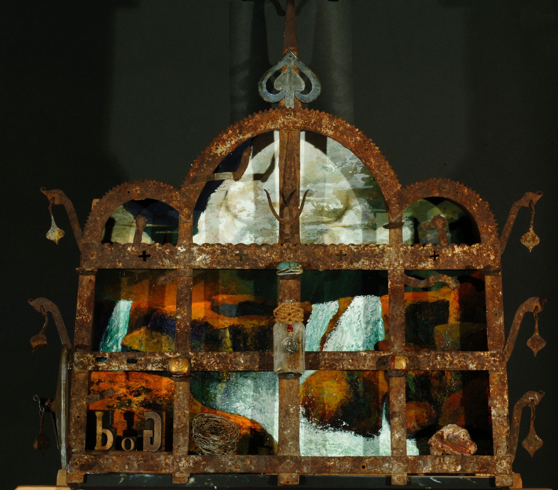 Rusty metal cage with arched top and stained glass panes, letters “b o j” visible.