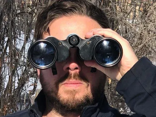 Man looking through binoculars outdoors, sunny, close-up.