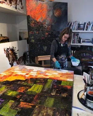 Woman in art studio working on large abstract paintings; mixing paint.