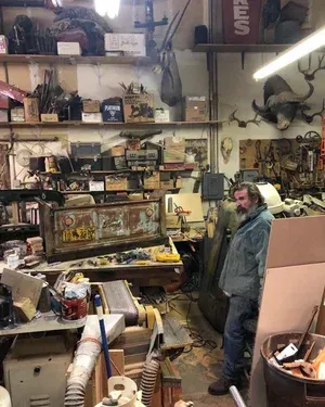Man in cluttered workshop with tools and animal skull.