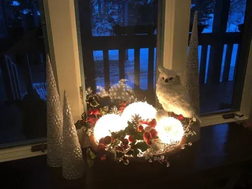 Holiday lights and decor by a window, including an owl, illuminated balls, and frosted trees.