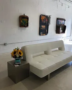 White couch with art pieces mounted above, sunflowers on a silver table.