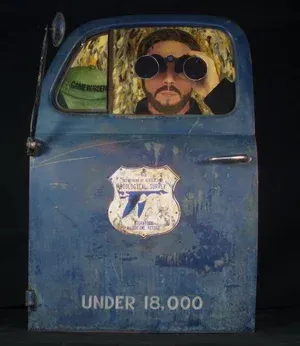 Man with binoculars peering through a blue truck door; a 