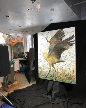 Painting of a sandhill crane with wings spread, set against a backdrop in an art studio.