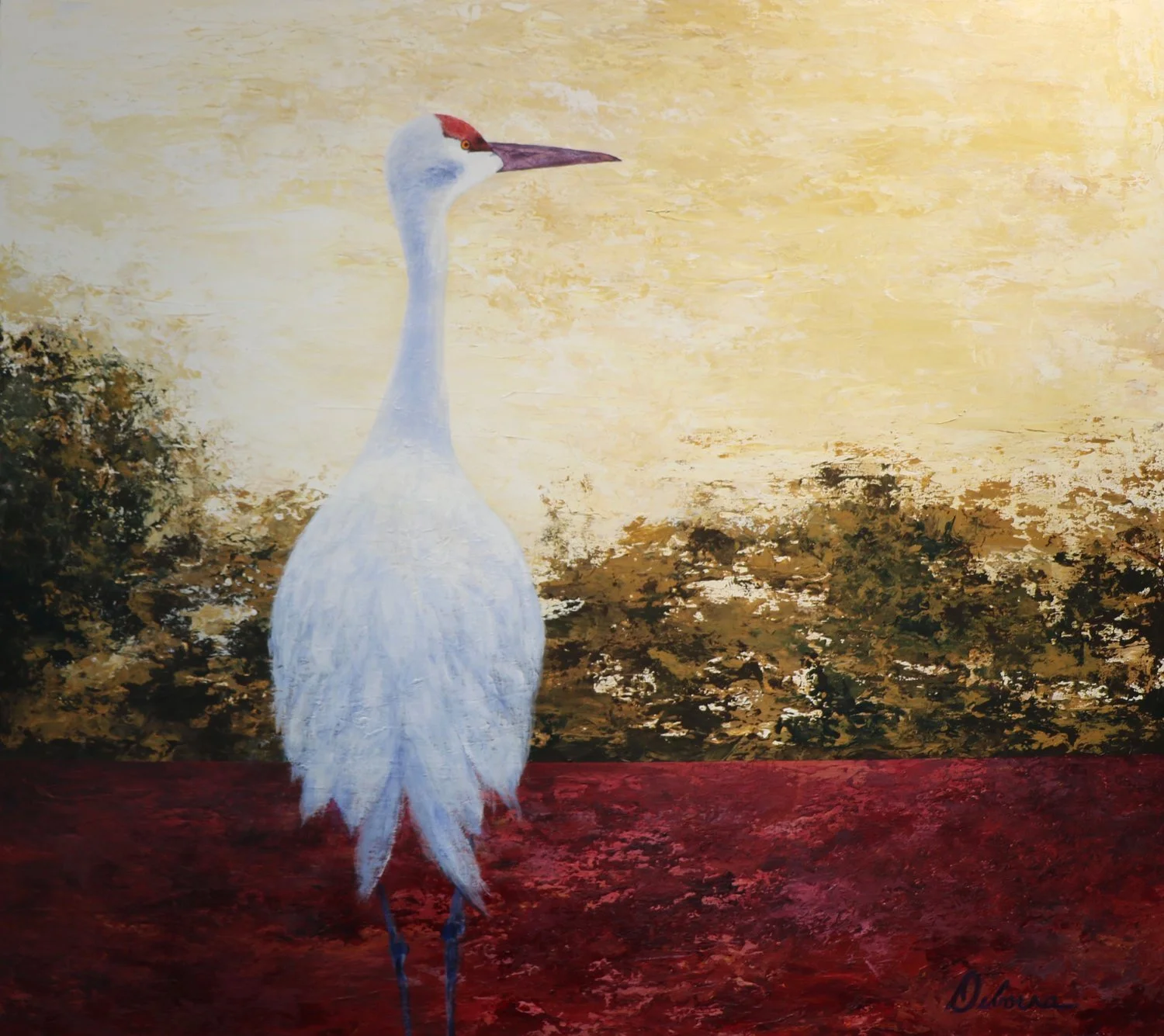 White sandhill crane with a red head stands in red water, gold sky behind it.