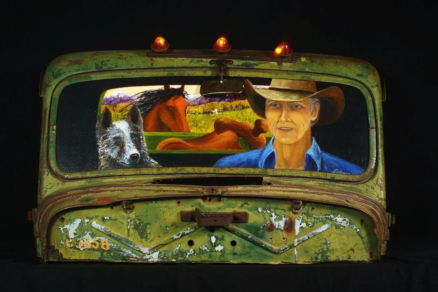 Green rusted truck cab with window showing a cowboy, horses, and a rural landscape.