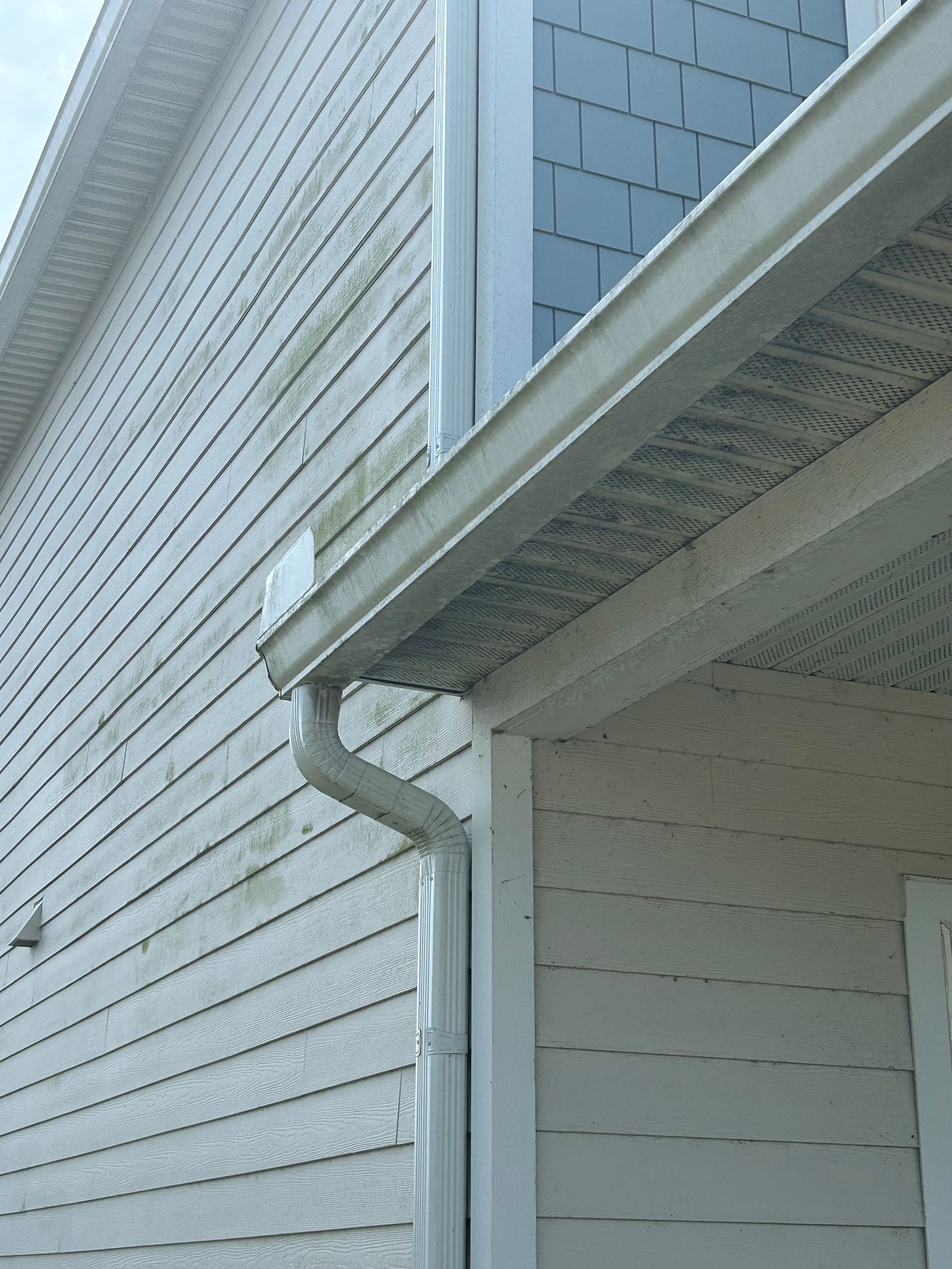 Gray ceiling of a porch with dark discoloration, viewed from below; part of a house and windows.