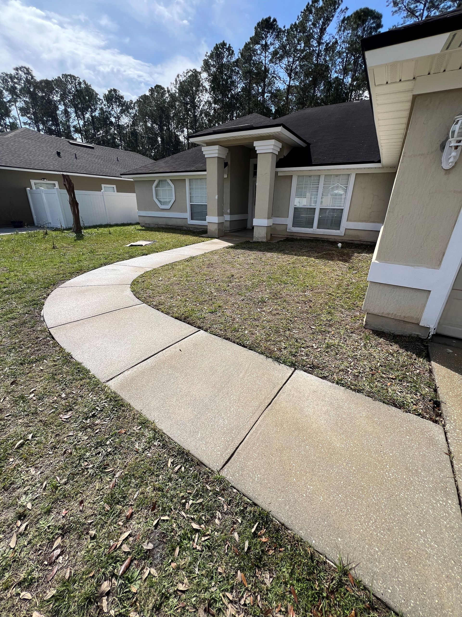 Sidewalk leading to a beige house with dark roof and windows, set in grassy yard.